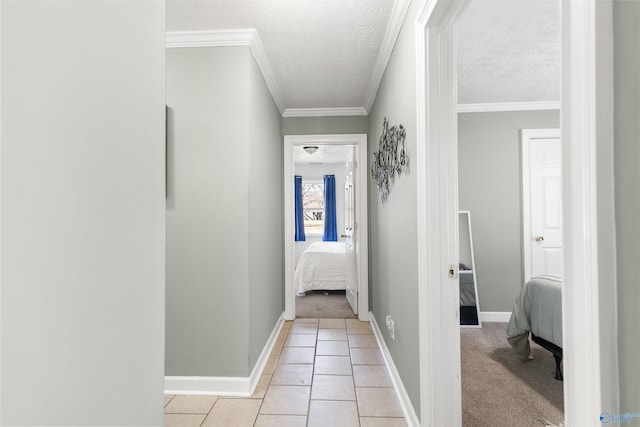 hallway featuring ornamental molding, light tile patterned flooring, a textured ceiling, and baseboards