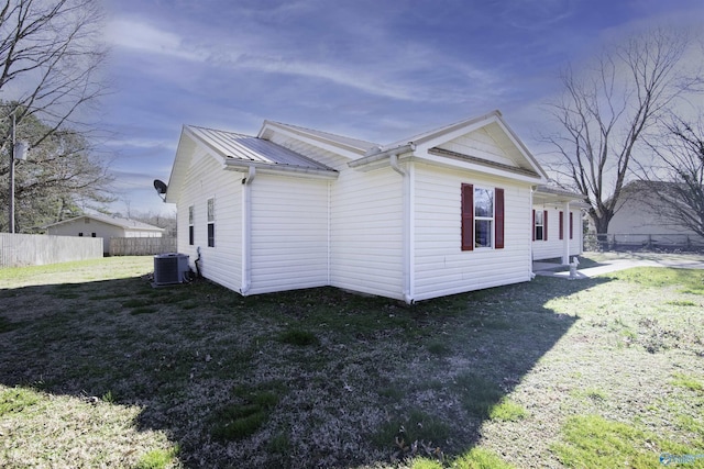 view of side of home with a yard, cooling unit, metal roof, and fence