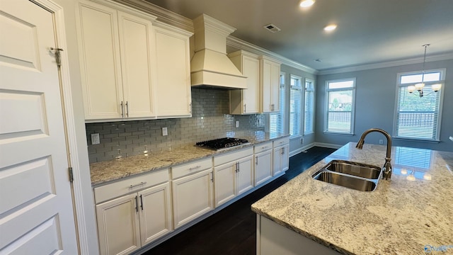 kitchen with a sink, stainless steel gas cooktop, dark wood finished floors, crown molding, and decorative backsplash