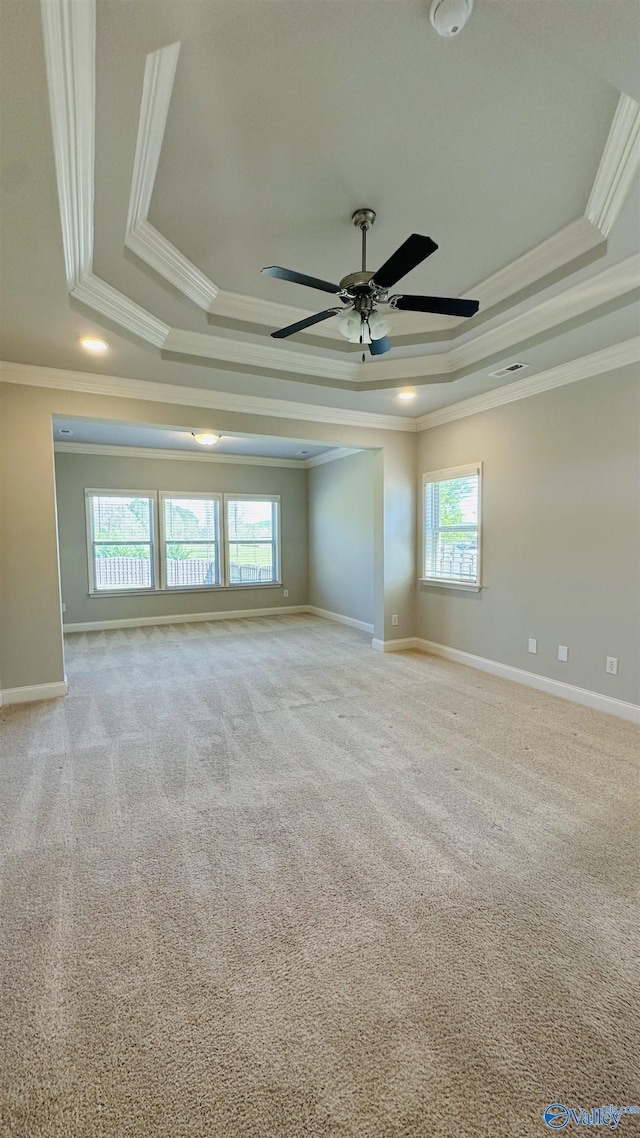 carpeted empty room featuring a raised ceiling, ornamental molding, a ceiling fan, and baseboards