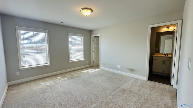 unfurnished bedroom featuring baseboards, carpet floors, a sink, and ensuite bath