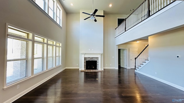unfurnished living room with stairway, a stone fireplace, a towering ceiling, wood finished floors, and a ceiling fan