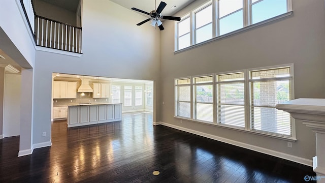 unfurnished living room featuring a ceiling fan, a towering ceiling, dark wood-type flooring, baseboards, and healthy amount of natural light