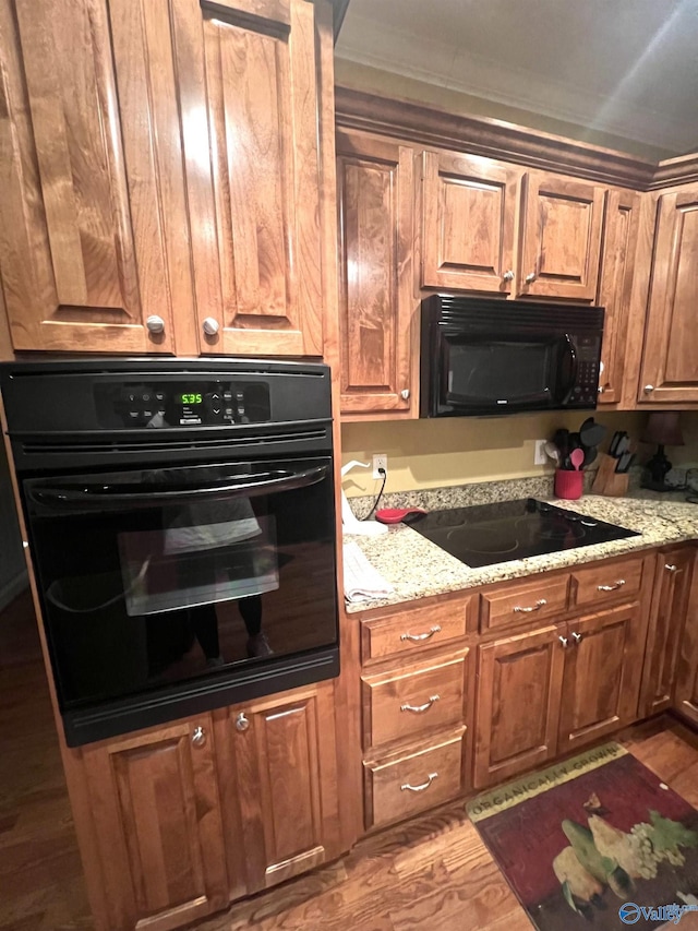 kitchen with light stone countertops, crown molding, black appliances, and hardwood / wood-style floors