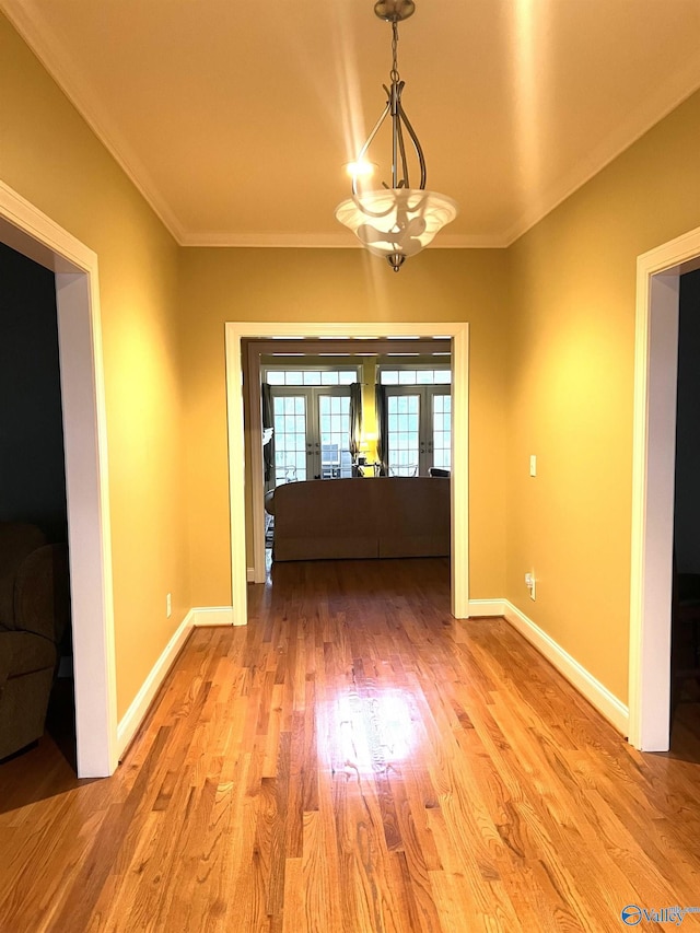 unfurnished dining area featuring an inviting chandelier, light hardwood / wood-style flooring, ornamental molding, and french doors