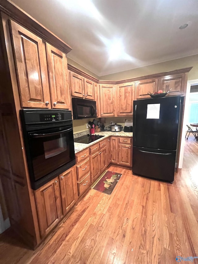 kitchen featuring light stone counters, light wood-type flooring, and black appliances