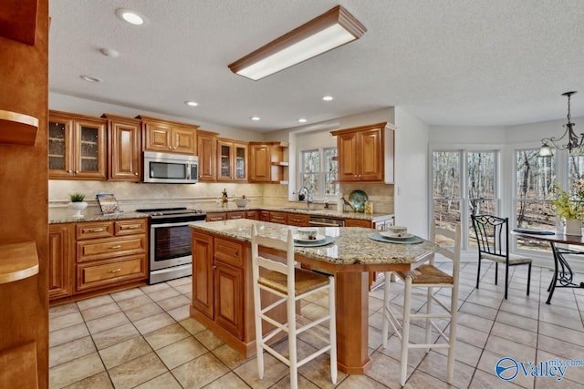 kitchen with a center island, a kitchen breakfast bar, sink, hanging light fixtures, and appliances with stainless steel finishes