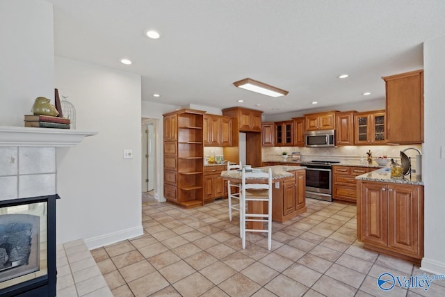 kitchen featuring a kitchen bar, tasteful backsplash, light stone counters, stainless steel appliances, and a kitchen island