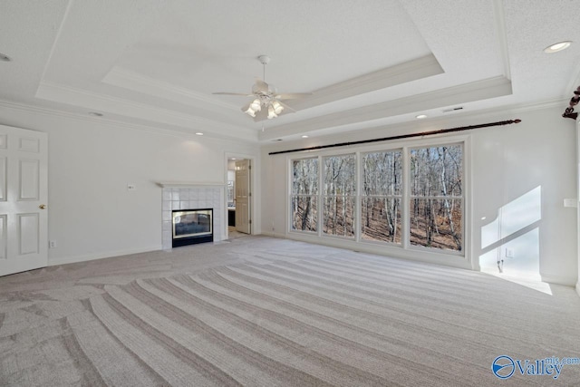 unfurnished living room featuring light carpet, a raised ceiling, crown molding, ceiling fan, and a tiled fireplace