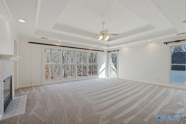 unfurnished living room with a raised ceiling, plenty of natural light, crown molding, and a tiled fireplace