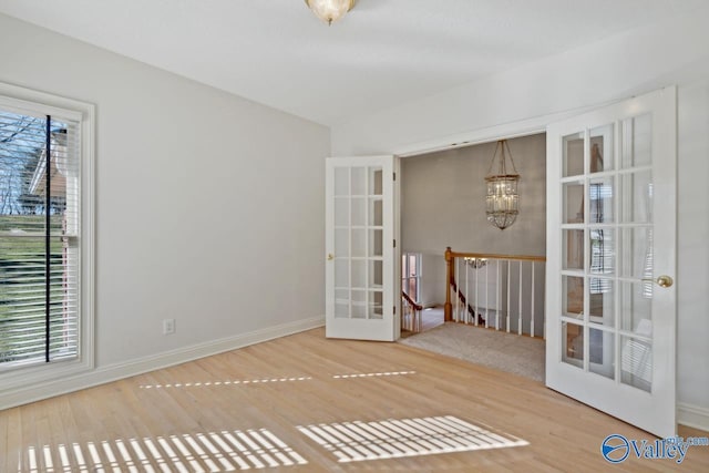 empty room with hardwood / wood-style floors, an inviting chandelier, and french doors