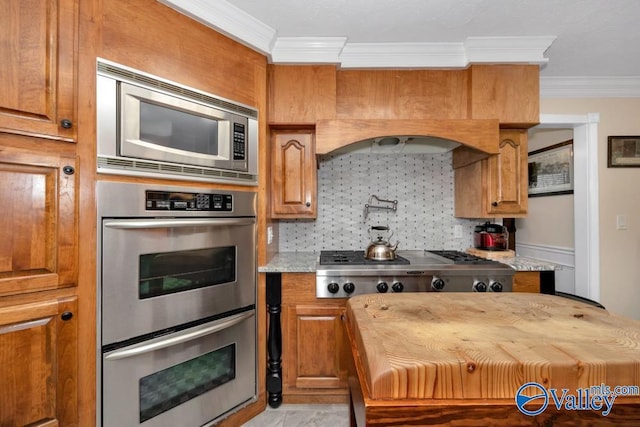 kitchen featuring crown molding, stainless steel appliances, light stone counters, and tasteful backsplash