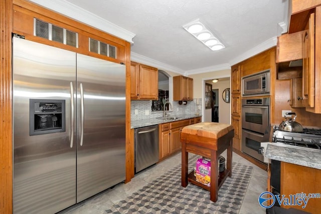 kitchen featuring sink, crown molding, stainless steel appliances, tasteful backsplash, and light stone countertops