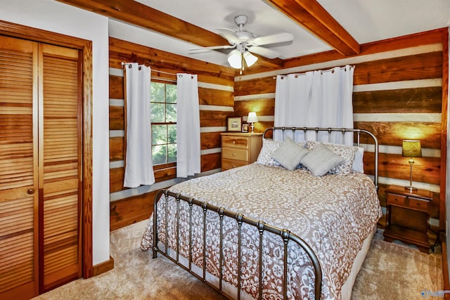 carpeted bedroom with a closet, beam ceiling, and ceiling fan