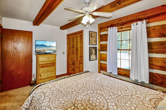 unfurnished bedroom featuring a closet, a textured ceiling, carpet flooring, beam ceiling, and ceiling fan