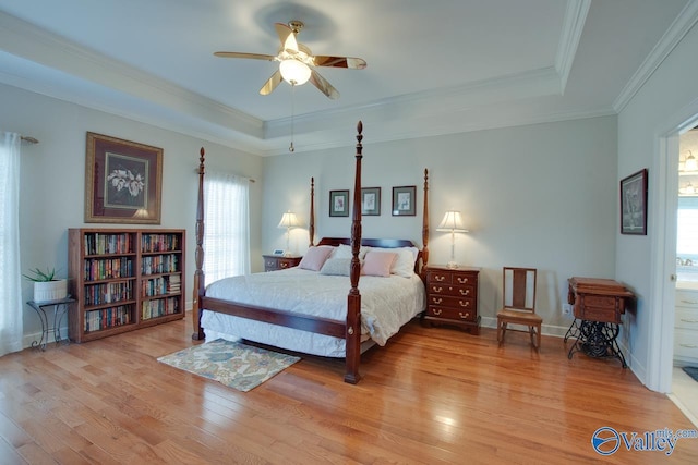 bedroom featuring light wood finished floors, baseboards, crown molding, and a tray ceiling