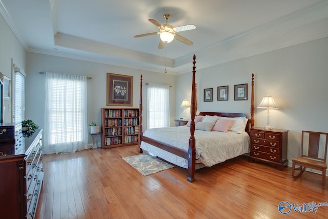 bedroom featuring a raised ceiling, a ceiling fan, light wood-style flooring, and crown molding