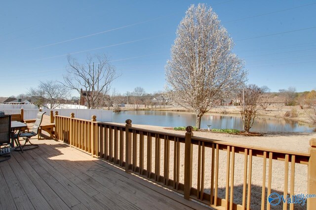 wooden terrace with outdoor dining area, a water view, and fence