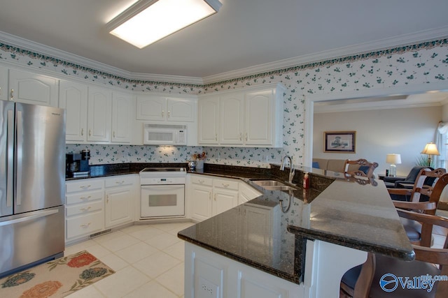 kitchen featuring white microwave, freestanding refrigerator, a sink, wall oven, and white cabinetry