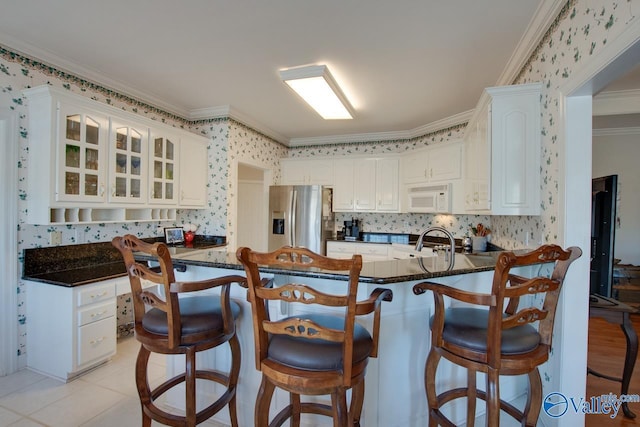 kitchen featuring white microwave, wallpapered walls, stainless steel fridge with ice dispenser, a peninsula, and a sink