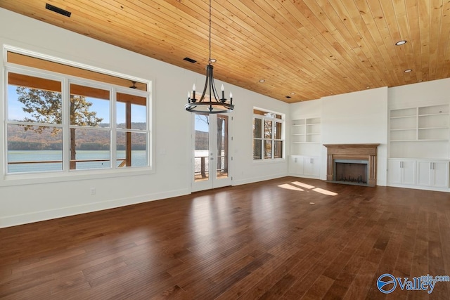 unfurnished living room featuring built in shelves, a water view, dark wood-type flooring, and a notable chandelier