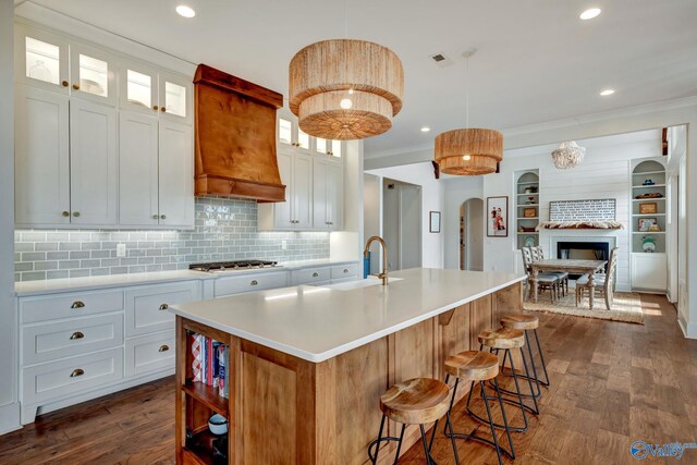 kitchen with white cabinets, a fireplace, a kitchen island with sink, dark wood-type flooring, and custom range hood