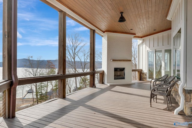sunroom / solarium with an outdoor brick fireplace, wooden ceiling, a water and mountain view, and a healthy amount of sunlight