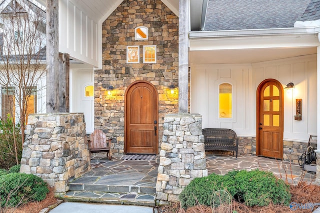 entrance to property featuring stone siding, a shingled roof, and a porch