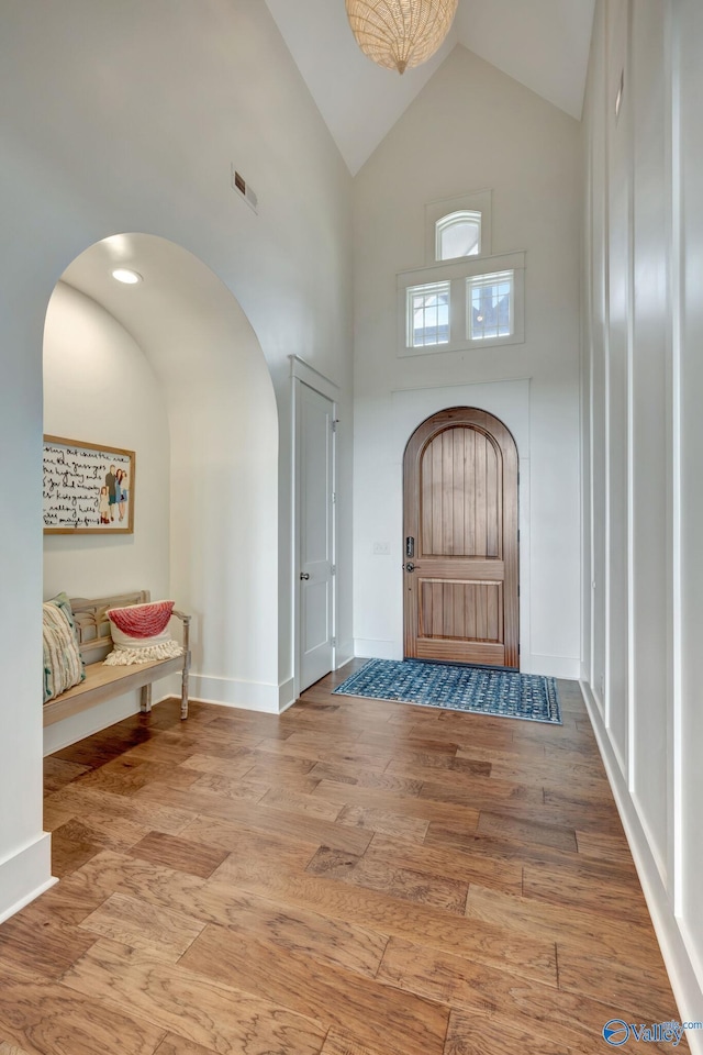 foyer entrance with arched walkways, high vaulted ceiling, wood finished floors, and visible vents