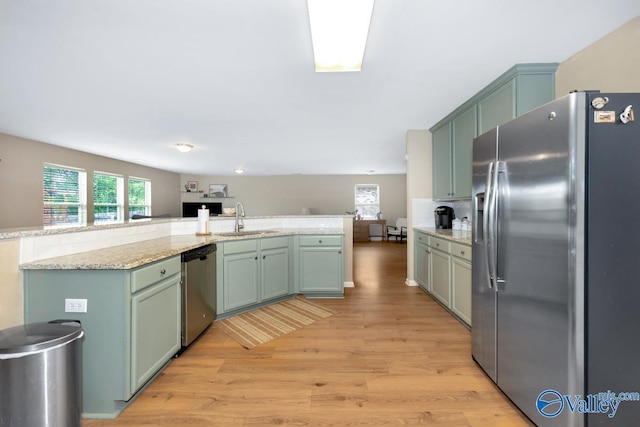 kitchen featuring stainless steel appliances, green cabinetry, a sink, and light wood finished floors