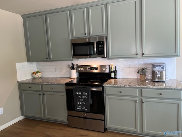 kitchen featuring light stone counters, stainless steel appliances, wood finished floors, baseboards, and decorative backsplash