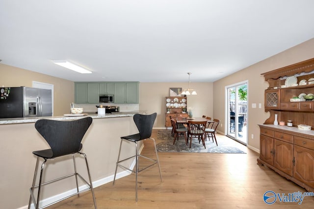 kitchen featuring a breakfast bar, green cabinets, stainless steel appliances, and hanging light fixtures