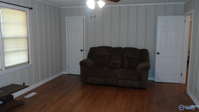 living area featuring a healthy amount of sunlight, ceiling fan, dark wood-type flooring, and ornamental molding