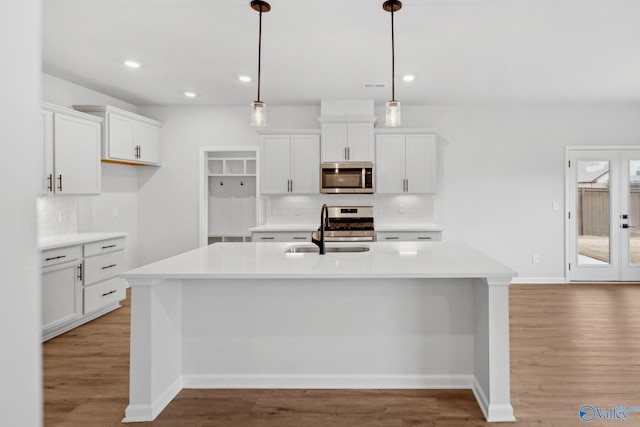 kitchen featuring sink, white cabinetry, a center island with sink, pendant lighting, and stainless steel appliances