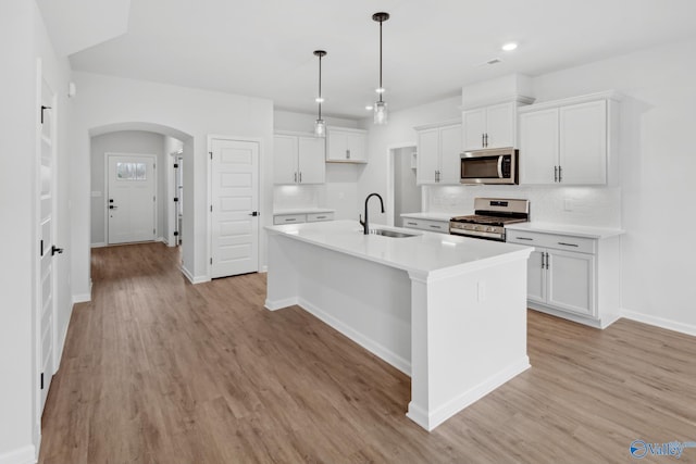 kitchen featuring appliances with stainless steel finishes, decorative light fixtures, sink, white cabinets, and a center island with sink