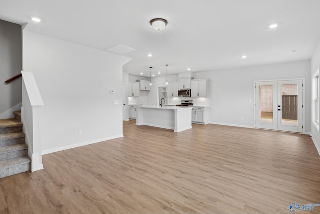 unfurnished living room with sink, french doors, and light wood-type flooring