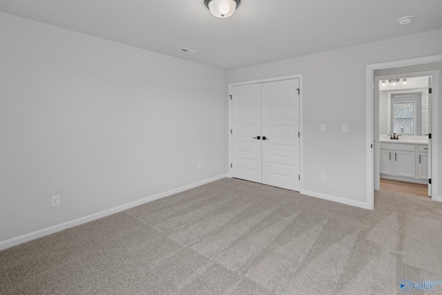 unfurnished bedroom with light carpet, a closet, ensuite bathroom, and sink