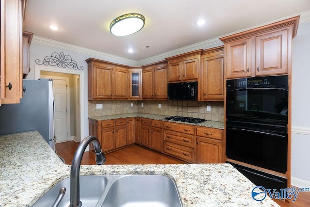 kitchen featuring light hardwood / wood-style floors, black appliances, sink, crown molding, and light stone countertops