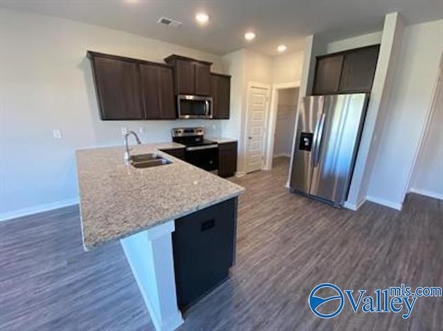 kitchen with sink, dark wood-type flooring, stainless steel appliances, dark brown cabinetry, and light stone countertops