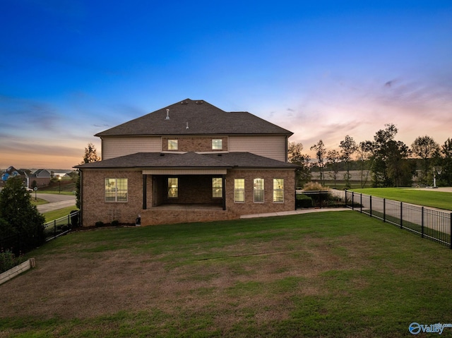 back of house at dusk featuring a yard, a fenced backyard, and brick siding