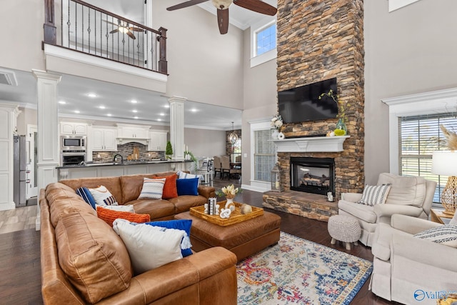 living area featuring crown molding, decorative columns, ceiling fan, a towering ceiling, and dark wood-style floors