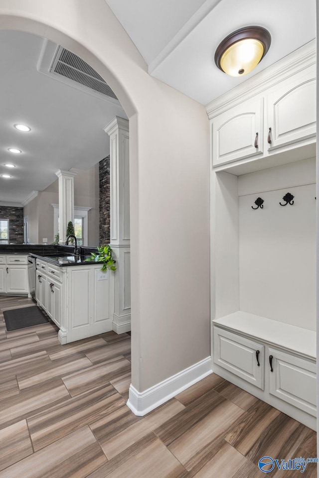 mudroom featuring baseboards, light wood-style floors, ornate columns, visible vents, and arched walkways