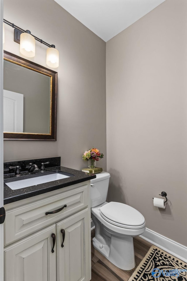 half bathroom with toilet, vanity, wood finished floors, and baseboards
