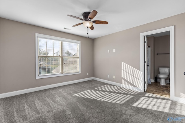 unfurnished bedroom featuring visible vents, baseboards, ceiling fan, carpet, and ensuite bath