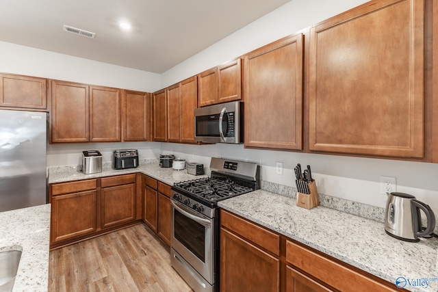 kitchen featuring light stone counters, appliances with stainless steel finishes, and light hardwood / wood-style flooring