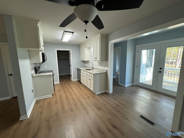 kitchen featuring sink, light wood-type flooring, black dishwasher, decorative backsplash, and white cabinets