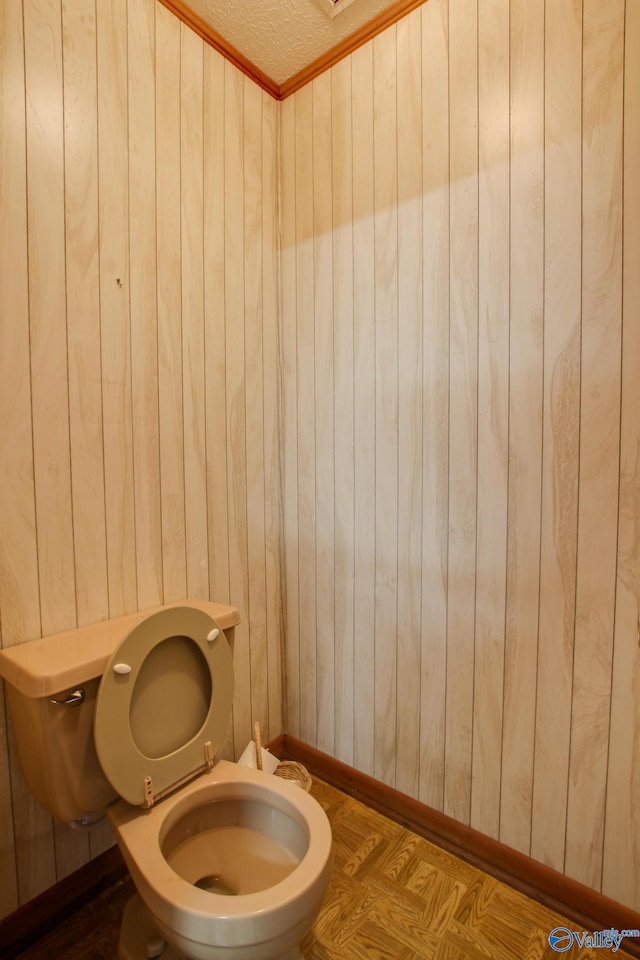 bathroom featuring wooden walls, toilet, and a textured ceiling