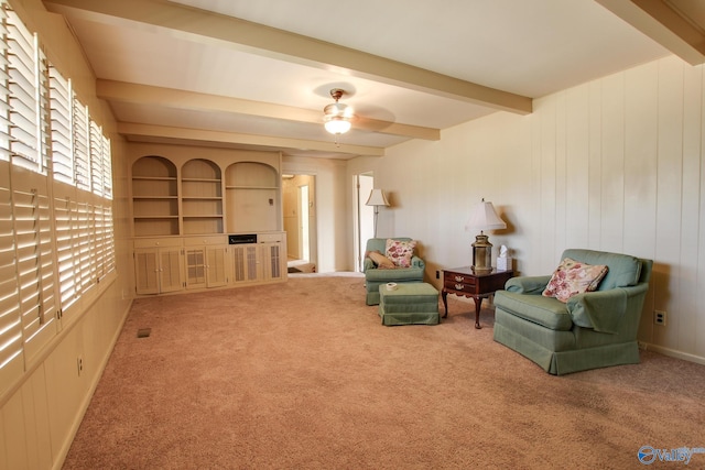 sitting room featuring ceiling fan, built in features, beamed ceiling, and carpet flooring