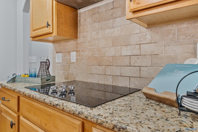 kitchen with black electric stovetop, decorative backsplash, and light stone countertops