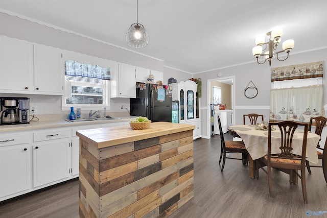 kitchen with white cabinets, dark hardwood / wood-style flooring, black fridge, ornamental molding, and decorative light fixtures